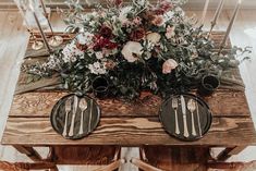 a wooden table topped with black plates and floral centerpieces on top of it