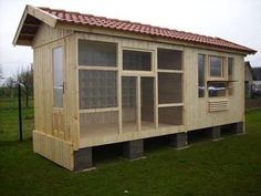 a small wooden structure with windows and a red roof in the middle of a grassy field