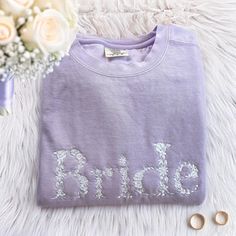 a bride sweatshirt with the word bride on it next to flowers and two pairs of earrings