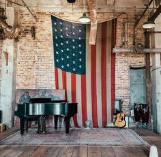 an american flag is hanging on the wall next to a piano in a room with brick walls