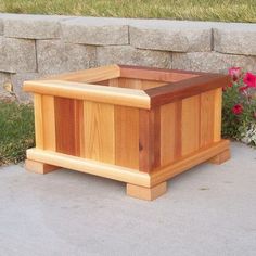 a wooden box sitting on top of a cement slab next to flowers and grass in front of a stone wall