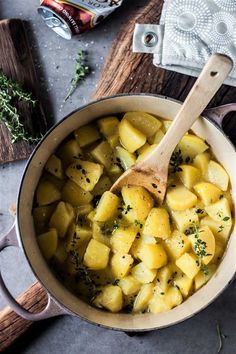 a pot filled with potatoes and herbs on top of a wooden cutting board next to an oven mitt