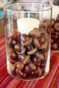 a candle that is sitting in some kind of glass cup filled with nuts on a table