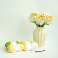 three balls of yarn next to a vase with flowers in it and two crochet hooks