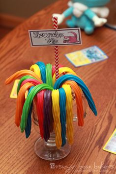 a glass filled with colorful candy canes sitting on top of a wooden table next to a sign