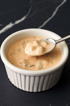 a white bowl filled with soup on top of a black counter next to a spoon