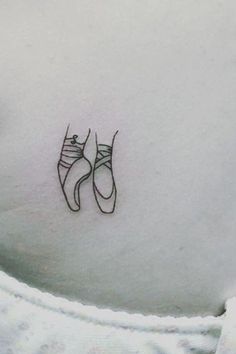 a pair of ballet shoes tattoo on the back of a woman's left shoulder