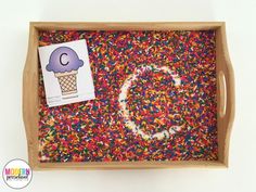 a wooden tray filled with sprinkles and a card on the bottom that says c