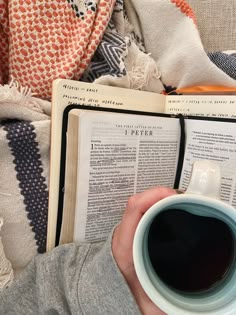 a person holding a cup of coffee and reading a book with an open book on it