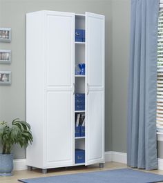 a white armoire with blue drawers in a room next to a potted plant