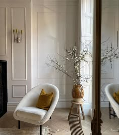 a living room with two chairs and a vase filled with flowers next to a mirror