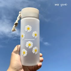 a hand holding a white and yellow water bottle with daisies painted on the side