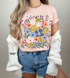 a woman with blonde hair wearing a pink flower t - shirt and blue denim shorts