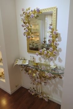 a mirror on the wall above a console with flowers and candles in it, along with other items