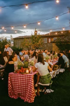 a group of people sitting around a table with food on it and lights strung overhead