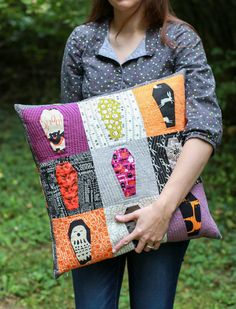 a woman holding an orange and purple patchwork pillow with halloween decorations on the front