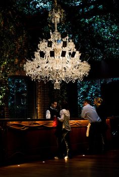 three people standing in front of a chandelier with lights hanging from the ceiling