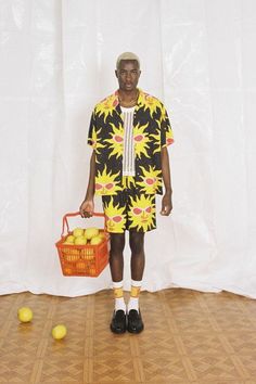 a man in yellow and black clothing holding a basket with lemons on the floor