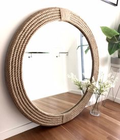 a round mirror sitting on top of a wooden floor next to a vase with flowers