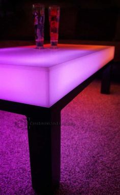 an illuminated table in the middle of a carpeted room with two shot glasses on it