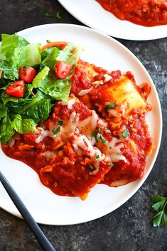 two white plates topped with lasagna covered in sauce and garnished with lettuce