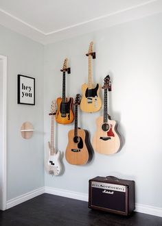 three guitars are hanging on the wall next to an amplifier and guitar case in a room