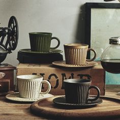 several coffee cups and saucers on a wooden table next to an old grinder