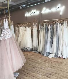 a room filled with lots of dresses and gowns hanging on clothes racks in front of a mirror