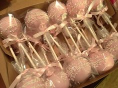 a box filled with pink cake pops covered in white sprinkles and bows