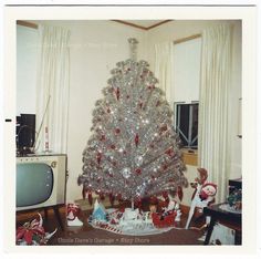 a silver christmas tree sitting in the middle of a living room next to a tv