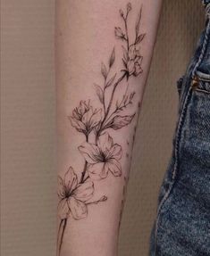 a black and white flower tattoo on the left inner arm, with small flowers growing out of it