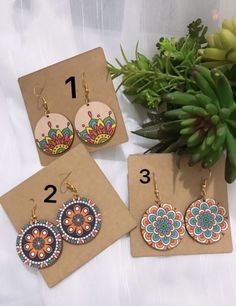 three pairs of earrings are on display next to a succulent plant and card