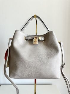 This stylish handbag is perfect for any occasion, whether you're traveling, attending a party, or simply running errands. With a rectangular shape and a light grey exterior color, it's both classic and versatile. The bag features a button and clasp closure, a crossbody strap, and a detachable strap for added convenience. Inside, you'll find cotton lining and several inner pockets to keep your belongings organized. The faux leather exterior material is accented with a button accent and gold-plated hardware for a touch of sophistication. This medium-sized bucket handbag is suitable for women and is 9 inches wide, 8 inches tall, and 5 inches deep. No matter where you're headed, this purse will be the perfect accessory to complete your outfit. Bucket Handbags, Grey Exterior, Satchel Bag, Shoulder Purse, Crossbody Strap, Satchel Bags, Cross Body Handbags, Running Errands, Bags Handbags