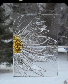 an image of a sunflower on a glass block in the snow with trees behind it