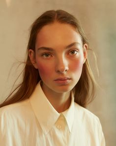 a woman with long hair wearing a white shirt and looking at the camera on her phone