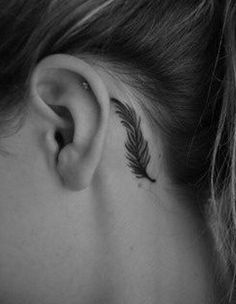 a woman's ear with a small feather tattoo on it