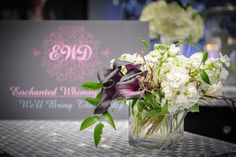 a vase filled with white and purple flowers on top of a metal table next to a sign