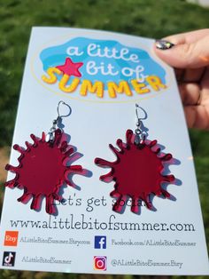 a person holding up a pair of earrings in front of a sign that says a little bit of summer