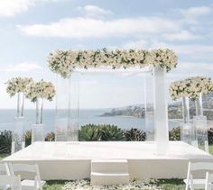 an outdoor ceremony setup with white flowers and greenery on the grass by the ocean