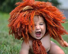 a baby wearing a lion costume laying on the grass with its mouth open and tongue out