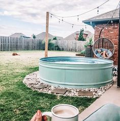 a person holding a cup in their hand near a pool with a hammock hanging over it