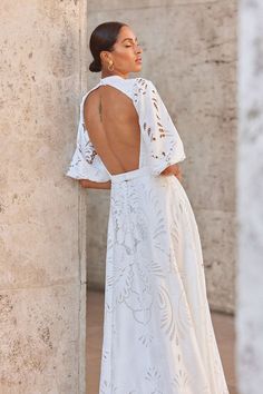 a woman leaning against a wall with her back turned to the camera and wearing a white dress