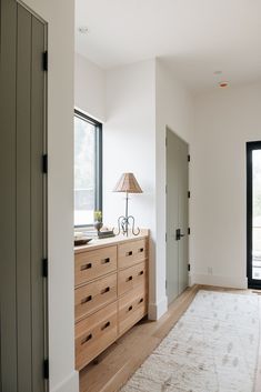 an empty room with a large white rug and wooden dresser next to a lamp on top of it