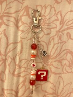 a red and white keychain with charms attached to it's sides on a fabric background