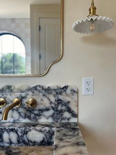 a bathroom sink with marble counter top and gold faucet, in front of a mirror