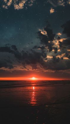 the sun is setting over the ocean with dark clouds and stars in the night sky