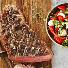 steak, salad and knife on a wooden cutting board next to a bowl of strawberries