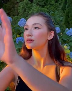 a woman is holding her hands up in front of some blue hydrangea flowers