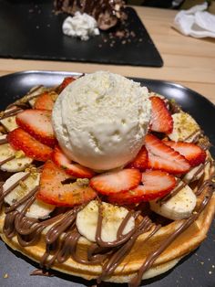 a waffle topped with strawberries, bananas and ice cream on a black plate