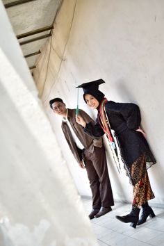 two people standing next to each other in front of a wall with a graduation cap on